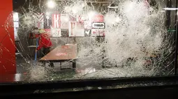 Seorang pria membersihkan dan terlihat melalui kaca yang rusak di sebuah restoran cepat saji yang dihancurkan dalam protes terhadap jam malam di Rotterdam, Belanda, Senin (25/1/2021). Lockdown di Belanda menahan warga untuk keluar rumah. Pelanggar bisa didenda 95 euro. (AP Photo/Peter Dejong)
