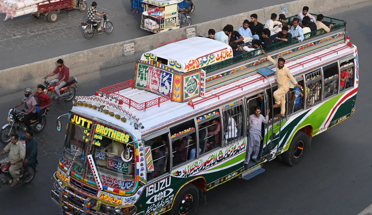 Sebuah bus dengan penumpang di atas atap berjalan di sepanjang jalan di Lahore pada 19 April 2023, saat orang-orang menuju kampung halaman mereka untuk merayakan Hari Raya Idul Fitri, yang menandai berakhirnya bulan puasa Ramadhan. (Photo by Arif Ali / AFP)