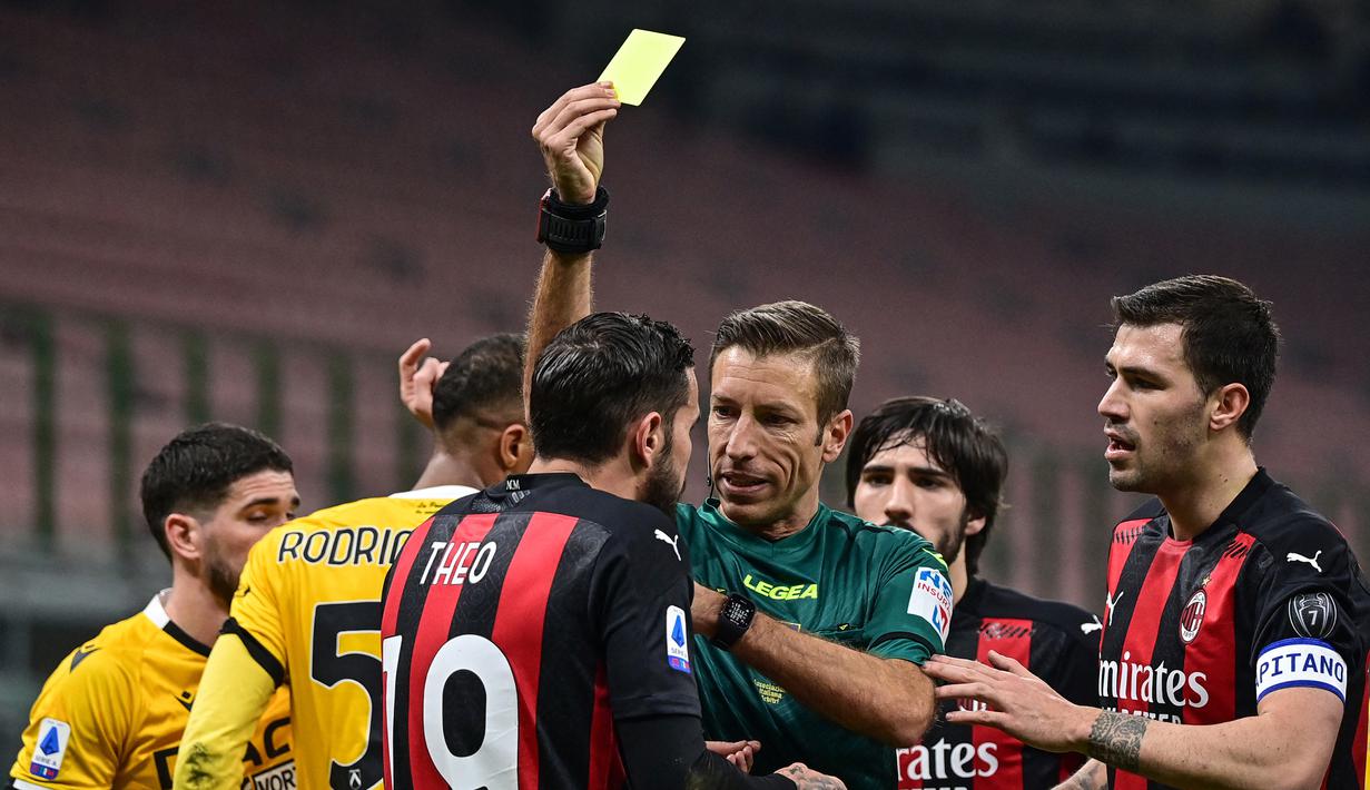 Wasit Davide Massa memberikan kartu kuning kepada bek AC Milan, Theo Hernandez saat menghadapi Udinese dalam laga lanjutan Liga Italia 2020/21 pekan ke-25 di San Siro Stadium, Rabu (3/3/2021). AC Milan bermain imbang 1-1 dengan Udinese. (AFP/Miguel Medina)