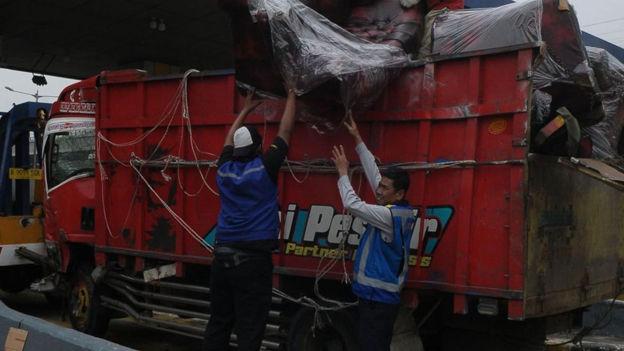 Petugas menaikkan muatan truk mebel yang berceceran setelah mengalami kecelakaan beruntun di depan Gerbang Tol Halim Utama, Jakarta, Rabu (27/3/2024). Foto: Merdeka.com/Imam Buhori