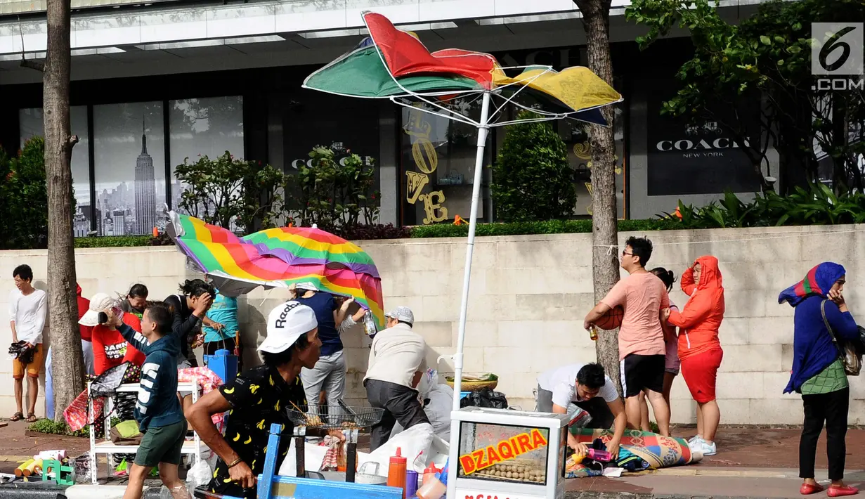 Payung milik pedagang terhembus angin kencang yang terjadi di sekitar Bundaran Hotel Indonesia, Jakarta, Minggu (26/11). Angin kencang dan gerimis terjadi saat kegiatan Hari Bebas Kendaraan, Minggu pagi. (Liputan6.com/Helmi Fithriansyah)