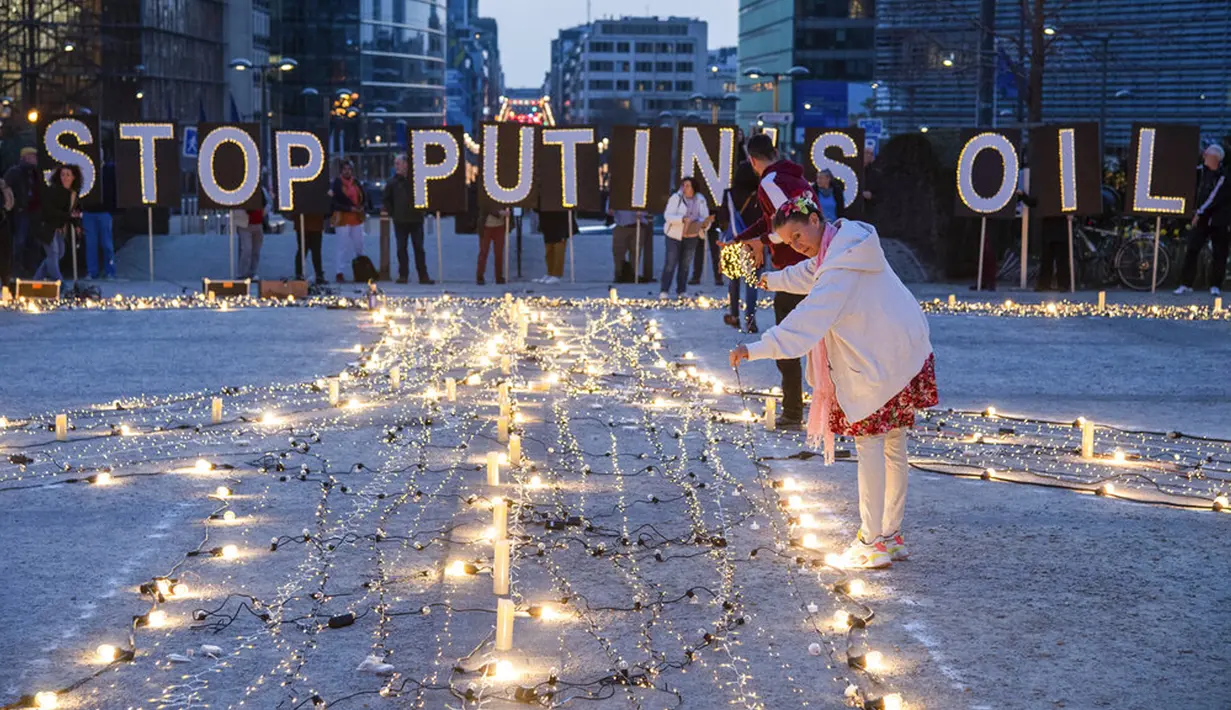 Seorang wanita berdiri dekat lampu dan lilin saat dinyalakan sekitar tanda perdamaian raksasa jelang KTT Uni Eropa dan NATO di Brussels, Belgia, 22 Maret 2022. Pengunjuk rasa meminta para pemimpin Uni Eropa memberlakukan larangan penuh terhadap bahan bakar Rusia. (AP Photo/Geert Vanden Wijngaert)