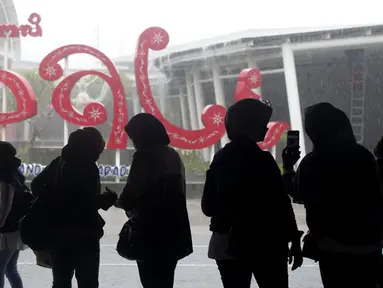 Warga berlindung dari hujan setibanya di Bandara Internasional Bali, Jumat (4/2/2022). Bali kembali dibuka untuk pelancong asing dari semua negara setelah penerbangan internasional dilanjutkan untuk pertama kalinya dalam dua tahun, tapi pengunjung tetap wajib karantina. (AP Photo/Firdia Lisnawati)