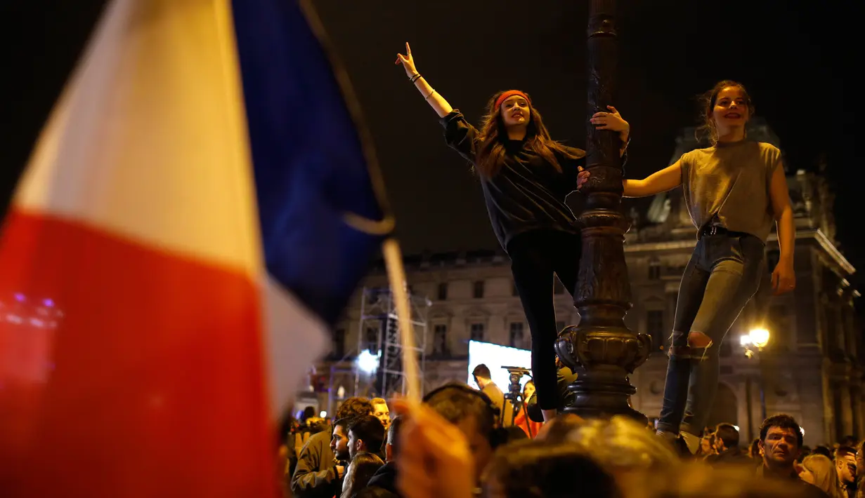 Dua orang wanita Prancis menari di lampu jalan museum Louvre, tempat Emmanuel Macron menyampaikan pidato kemenangannya, di Paris, Minggu (7/5). Emmanuel Macron mendapatkan suara tertinggi pada pemilihan presiden putaran kedua. (AP Photo/Laurent Cipriani)