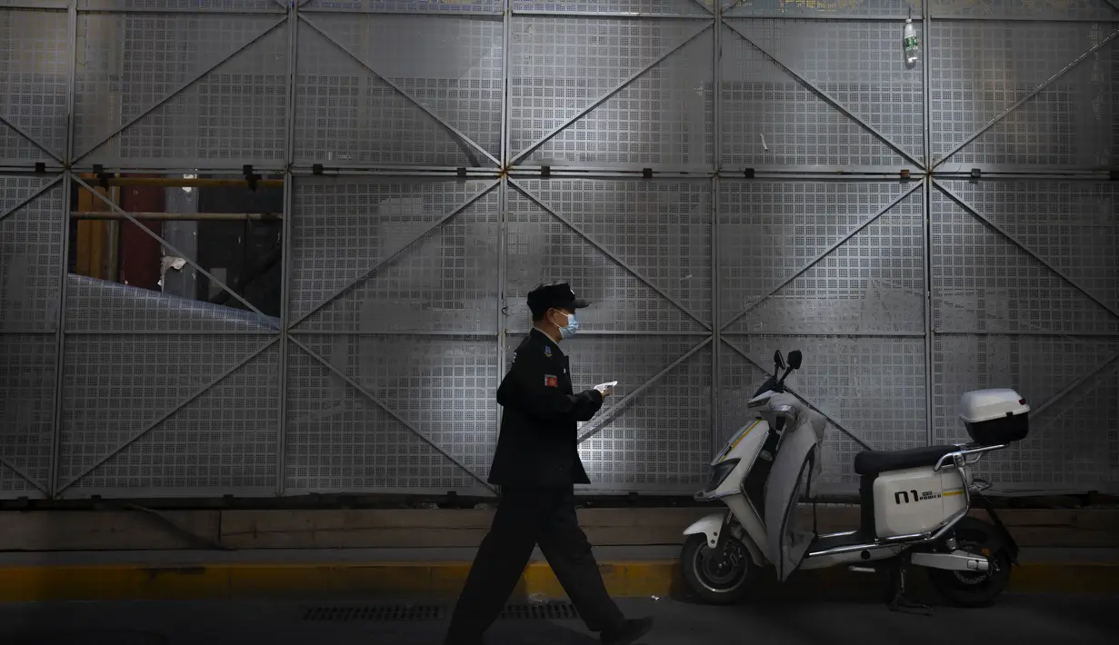 Seorang penjaga keamanan yang mengenakan masker berjalan melewati lokasi konstruksi di Beijing, Selasa (11/10/2022). Lockdown di China dilakukan setelah jumlah kasus Covid-19 harian baru meningkat tiga kali lipat setelah liburan selama seminggu, menjelang pertemuan besar Partai Komunis di Beijing minggu depan. (AP Photo/Mark Schiefelbein)