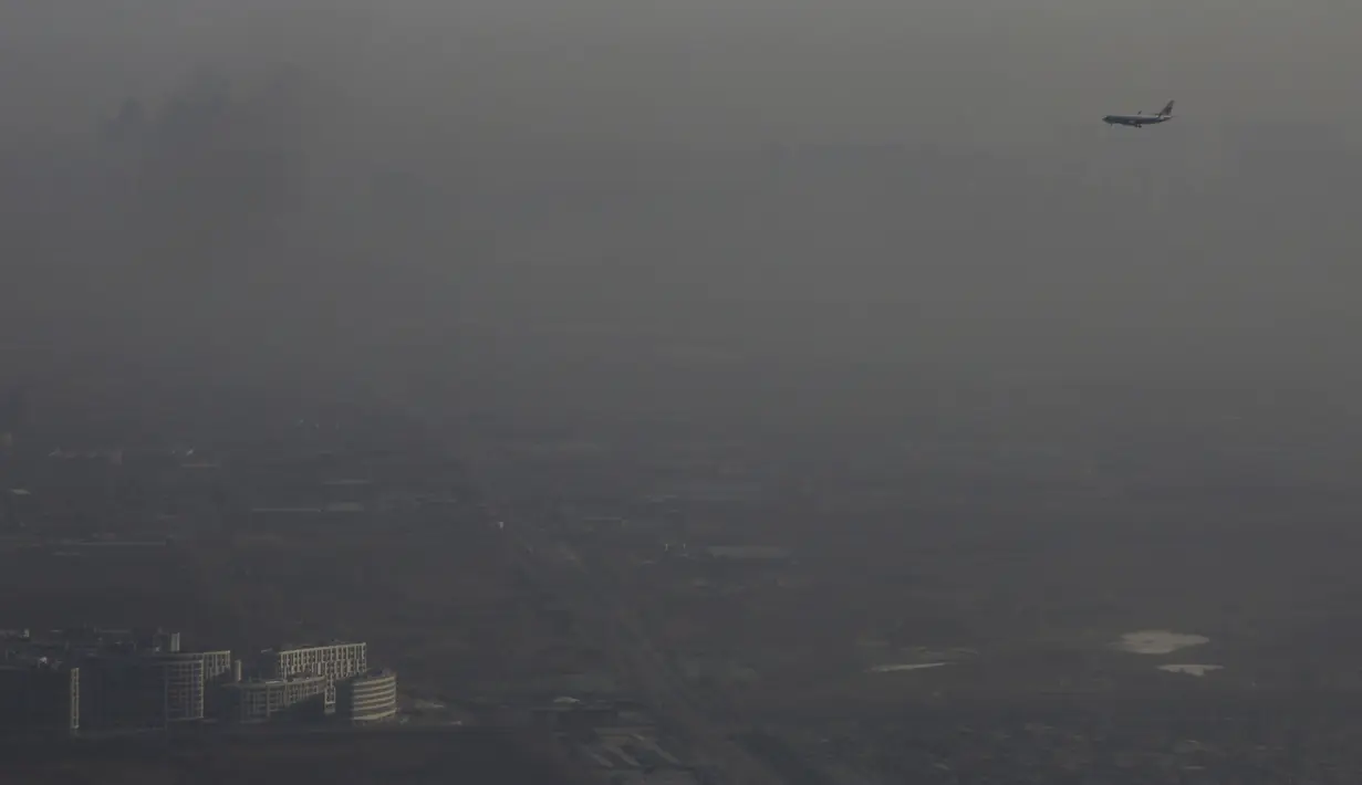 Sebuah pesawat melintas di tengah kabut asap tebal yang menyelimuti Beijing, Cina, 2 Januari 2017. Kabut tebal ini membuat sejumlah warga mengunakan masker saat beraktivitas. (Reuters/Jason Lee)