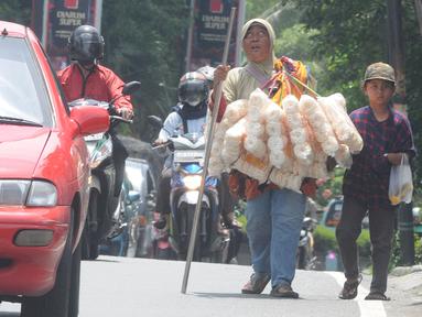 Penyandang tunanetra Ibu Adel (48) berjalan bersama anak bungsunya menyusuri jalan raya Ciputat, Tangerang Selatan, Selasa (26/04/20222). Warga Pondok Cabe 3 ini setiap harinya menyusuri jalan hingga sekitar 10 km menjajakan kerupuk Bangka yang dijualnya Rp 25 ribu/bungkus. Sudah beberapa bulan terakhir ini ia mengaku pendapatannya merosot drastis hanya sekitar Rp 50 ribu/ hari yang digunakan untuk mencukupi kebutuhan sehari-hari. (merdeka.com/Arie Basuki)