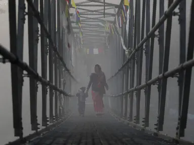 Seorang wanita Nepal menyusuri jembatan bersama anaknya untuk mengikuti festival Gaya Aunsi di Kathmandu, Nepal (21/12). Ritual suci ini digelar untuk memberi doa dan penghormatan kepada anggota keluarga yang telah meninggal. (AP Photo/Niranjan Shrestha)