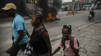 Orang-orang berjalan di sekitar ban yang dibakar oleh pengunjuk rasa untuk menuntut Perdana Menteri Haiti Ariel Henry mundur dan menyerukan kualitas hidup yang lebih baik, di Port-au-Prince, Haiti, Senin (29/8/2022). (AP Photo/Odelyn Joseph)