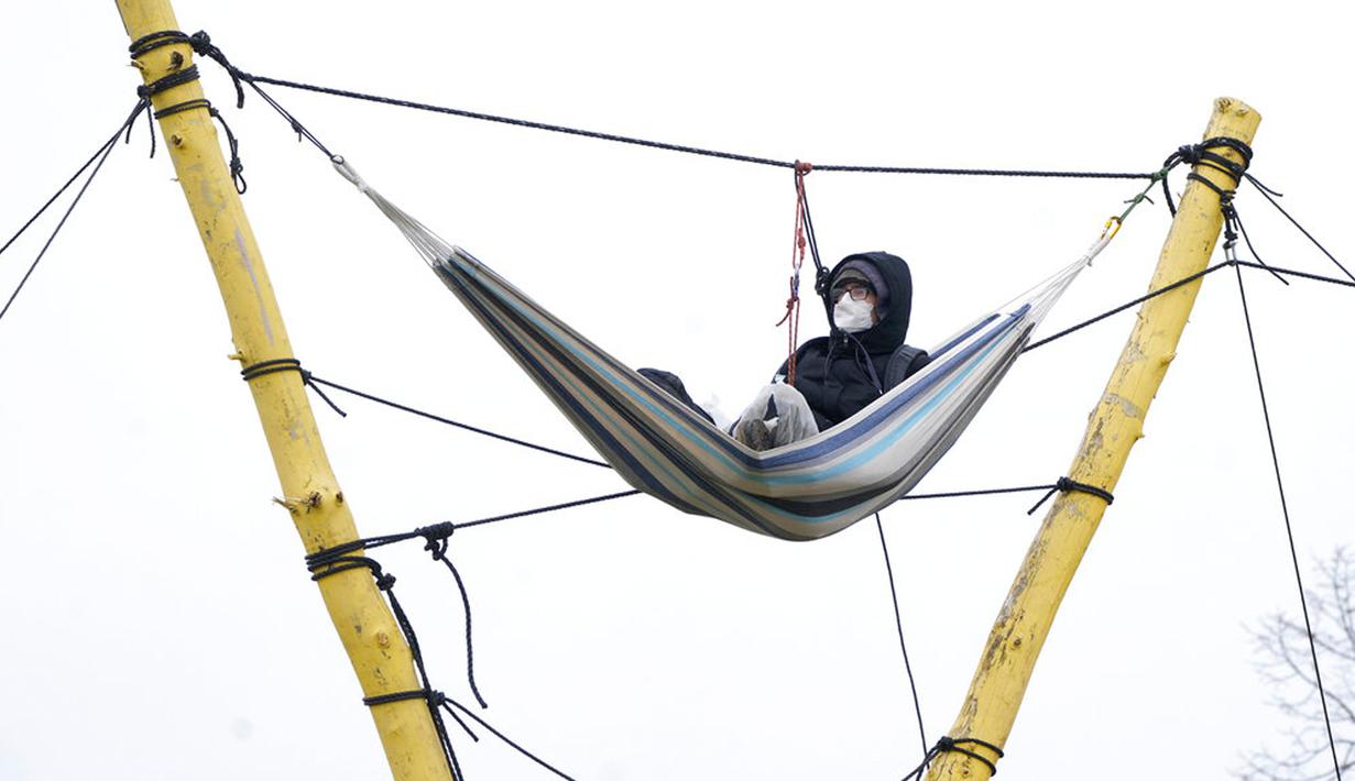 Seseorang duduk di tempat tidur gantung di sebelah tambang batu bara Garzweiler di Desa Luetzerath dekat Erkelenz, Jerman, 10 Januari 2023. Pengadilan Jerman menolak upaya terakhir para aktivis iklim untuk tinggal di desa yang ditinggalkan untuk perluasan tambang batu bara sehingga menjadi medan pertempuran antara pemerintah dan pencinta lingkungan. (AP Photo/Michael Probst)