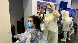 Seorang penata rambut mengenakan masker memotong rambut pelanggannya di sebuah pusat kecantikan wanita di Riyadh, Arab Saudi (21/6/2020). Pemerintah Arab Saudi mulai membuka kembali kegiatan perekonomian setelah melonggarkan lockdown Covid-19. (AFP Photo/Rania Sanjar)