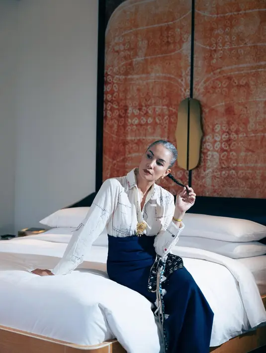 Duduk di kasur, Nadya Hutagalung kenakan kemeja print dan wrapped skirt navy blue dengan sentuhan Batik [@nadyahatugalung]