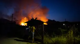 Para lelaki menutup pintu ketika api membakar di dekat desa Galataki, dekat Korintus, Yunani, Rabu, (22/7/2020). Pemerintah Yunani mengevakuasi lima pemukiman sebagai tindakan pencegahan. (AP Photo/Petros Giannakouris)