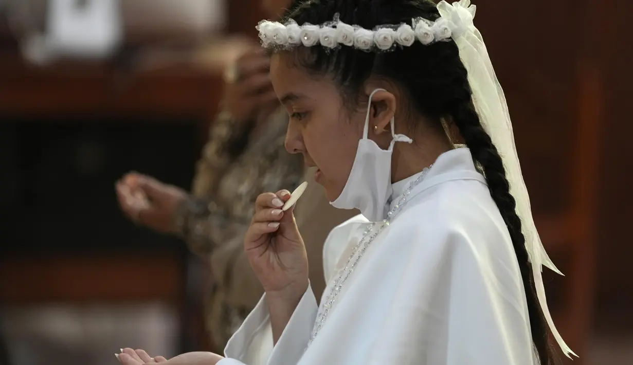 Seorang gadis makan wafer selama upacara Perjamuan Kudus pertama di tengah pandemi virus corona baru di gereja Katolik Nuestra Senora de la Merced di Lima, Peru, Jumat (3/12/2021). (AP Photo/Martin Mejia)