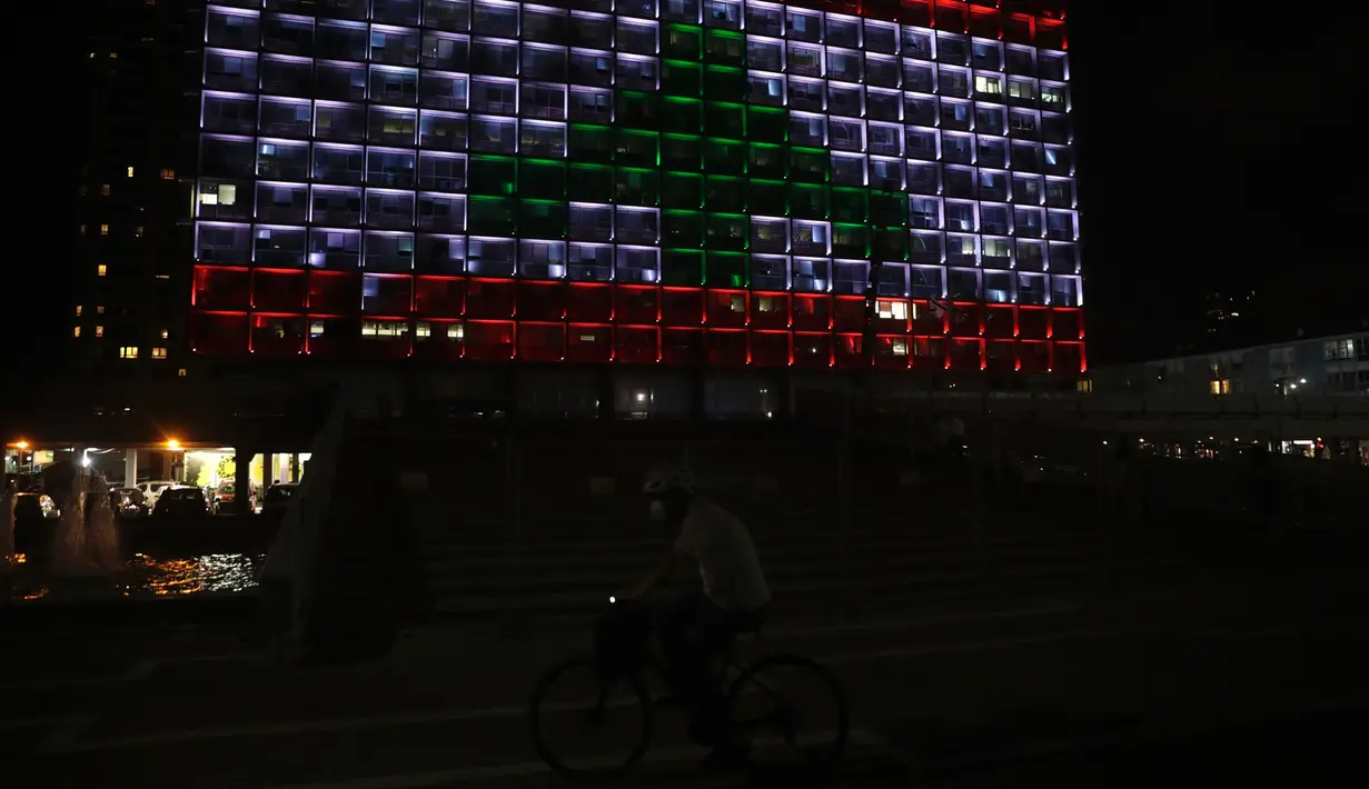 Seorang pria Israel bersepeda saat gedung Balai Kota diterangi dengan bendera Lebanon di Tel Aviv, Rabu (5/8/2020). Cahaya bendera Lebanon diproyeksikan sebagai bentuk solidaritas atas ledakan dahsyat di Beirut yang menghebohkan dunia. (AP Photo/Sebastian Scheiner)