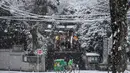 Seorang pekerja layanan pengiriman mengendarai sepeda melewati kuil Shinto saat salju turun di Tokyo, Kamis (6/1/2022). Pusat Tokyo dan kota Tsukuba, Prefektur Ibaraki, mencatat 3 sentimeter salju, sementara Chiba dan Yokohama memiliki 2 cm salju. (AP Photo/Kiichiro Sato)