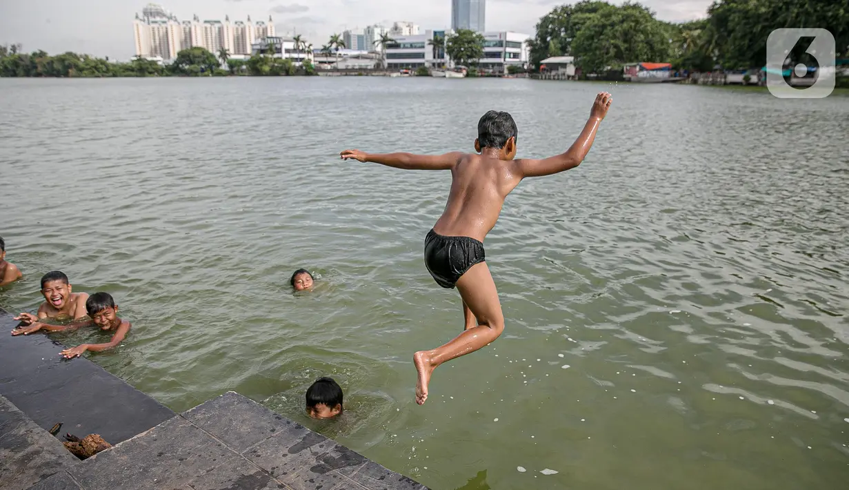 Seorang anak melompat di Danau Sunter, Jakarta, Selasa (2/2/2021). Minimnya lahan bermain anak membuat mereka memanfaatkan tempat yang tidak semestinya untuk bermain karena adanya risiko hanyut dan tenggelam bila tidak mampu untuk berenang. (Liputan6.com/Faizal Fanani)