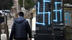 Seorang pria berjalan melewati makam Yahudi yang dicoret simbol Nazi di pemakaman Yahudi, Quatzenheim, Prancis, Selasa (19/2). Aksi vandalisme ini dilakukan terhadap sekitar 80 makam. (Frederick FLORIN/AFP)