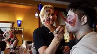 Seorang pria merias wajah rekannya untuk menyerupai zombie untuk menyambut halloween di Amerika, Minggu (18/10/2015). Tradisi Halloween berasal dar Irlandia yang dibawa hingga Amerika Serikat. (REUTERS/Shannon Stapleton)