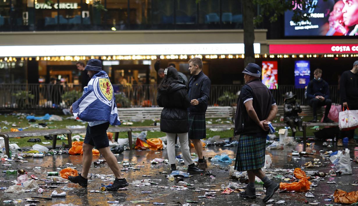 Penggemar Skotlandia berjalan di antara sampah yang ditinggalkan oleh penggemar yang berpesta sebelum pertandingan grup D kejuaraan sepak bola Euro 2020 antara Inggris dan Skotlandia, di London, Jumat (18/6/2021).  (AFP/Tolga Akmen)
