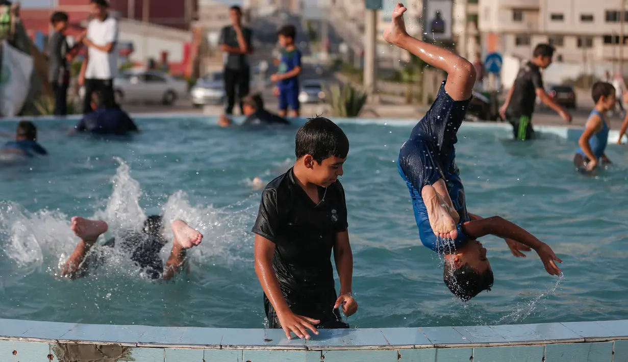 Anak-anak Palestina bermain di air mancur umum selama hari musim panas di Kota Gaza (20/7/2020). Musim panas yang terjadi di Palestina membuat anak-anak memenuhi air mancur. Mereka berupaya mendinginkan tubuh mereka dengan cara berenang di air mancur tersebut. (AFP Photo/Mahmud Hams)