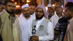 Jemaah haji berbincang dengan seorang penerjemah di kota suci Islam, Makkah, Arab Saudi, 17 Agustus 2018. Para penerjemah ini bisa dicirikan dengan pria yang memakai rompi abu-abu, dan di dadanya dibordir nama bahasa yang dia kuasai. (AFP/AHMAD AL-RUBAYE)