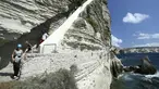Turis menuruni tangga Raja Aragon di Bonifacio di pulau Corsica, Mediterania Prancis (19/9/2021). Menurut legendanya, Tangga Raja Aragon, sebuah monumen bersejarah Corsica, digali dengan tangan di tebing batu kapur di suatu malam oleh pasukan Raja Aragon tahun 1420. (AFP/Pascal Pochard-Casabianca)
