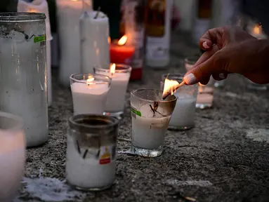 Seorang wanita menyalakan lilin untuk memberikan penghormatan kepada para korban tewas di depan klub malam Jet Set di Santo Domingo, Dominika pada 11 April 2025. (MARTIN BERNETTI/AFP)