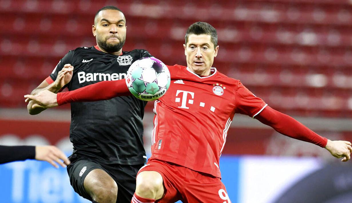 Striker Bayern Munchen, Robert Lewandowski, berebut bola dengan pemain Bayer Leverkusen, Jonathan Tah, pada laga Bundesliga di Stadion BayArena, Minggu (20/12/2020). Bayern Munchen menang dengan skor 2-1. (Bernd Thissen/Pool Photo via AP)