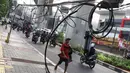 Pejalan kaki melintasi trotoar yang terhalang instalasi kabel di Jalan Kyai Maja, Jakarta, Rabu (10/4). Selain menganggu kenyamanan pejalan kaki, kondisi instalasi kabel yang semrawut tersebut juga berbahaya apabila mengandung aliran listrik. (Liputan6.com/Immanuel Antonius)
