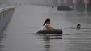 Seorang anak perempuan bermain ban saat banjir melanda Xinxiang, Provinsi Henan, Tiongkok, (9/7). Sedikitnya 420 ribu warga dari 4 kota setempat, termasuk ibukota Fuzhou terpaksa dievakuasi ke tempat yang lebih aman. (REUTERS)