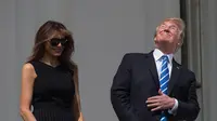Presiden AS Donald Trump bersama Ibu Negara, Melania Trump menyaksikan  gerhana matahari dari balkon Gedung Putih di Washington, Senin (21/8). Trump tertangkap kamera menyaksikan fenonema langka tersebut tanpa kacamata pelindung. (NICHOLAS KAMM/AFP)