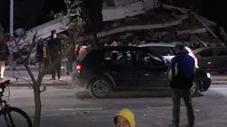 Seorang pria berbicara di ponsel ketika yang lain melihat kerusakan bangunan setelah gempa bumi di Durres,  Albania barat, Selasa (26/11/2019). Gempa bumi bermagnitudo 6,4 mengguncang Albania, Selasa dini hari yang menyebabkan beberapa bangunan dan gedung permukiman runtuh. (AP Photo)