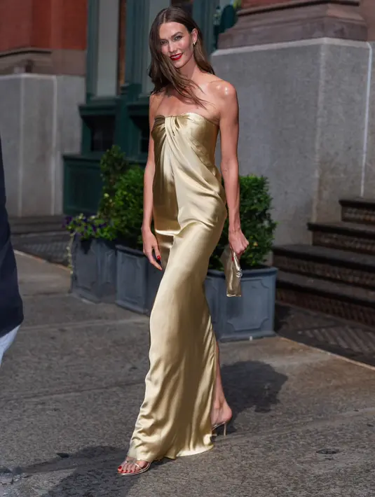 Karlie Kloss, memilih pendekatan understated namun tetap mewah. Ia mengenakan gaun strapless berbahan satin berwarna champagne gold dengan detail draping di bagian dada. Potongan slip dress yang jatuh mengikuti lekuk tubuh dipadukan clutch senada, sandal bertali tipis, serta lipstik merah klasik yang memberi sentuhan old Hollywood glamour.