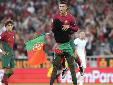 Ada momen menarik yang terjadi pada laga Kualifikasi Euro 2024 antara Portugal menghadapi Bosnia Herzegovina di Luz Stadum, Lisbon, Portugal, Minggu (18/6/2023) dini hari WIB. Di tengah laga, seorang penyusup lapangan memasuki arena pertandingan sambil mengibarkan bendera Portugal. Tak cuma berlari, pemuda berbadan kurus tersebut pun menghampiri Cristiano Ronaldo, lantas memperagakan selebrasi ikonik "siuuu" di depan sang megabintang. Bahkan sang penyusup sempat mengangkat CR-7 ke udara sebelum akhirnya ia kembali berlari menghindari kejaran petugas keamanan, hingga akhirnya ia menghentikan aksinya di pinggir lapangan sambil melakukan selebrasi "siuuu". (AP Photo/Armando Franca)