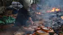 Seorang pria mengenakan masker gas saat memasak ikan di pot tanah liat menggunakan kayu bakar di provinsi Ha Nam, Vietnam, Selasa (21/1/2020). Ikan rebus adalah makanan lezat populer untuk Tahun Baru Imlek atau dikenal dengan nama Tet di utara Vietnam. (Nhac NGUYEN / AFP)