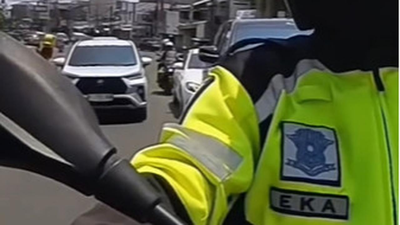 Seorang polisi pengawal menegur pengemudi sedan mewah bandel yang nekat mengikuti konvoi pejabat saat membelah kemacetan.