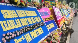 Pejalan kaki melintasi karangan bunga untuk terdakwa Hendra Kurniawan di depan Pengadilan Negeri Jakarta Selatan, Senin (27/2/2023). Karangan bunga itu terus berdatangan dan disusun bertumpuk-tumpuk, bahkan menutupi ruas trotoar yang berada tepat di depan PN Jaksel. (Liputan6.com/Angga Yuniar)
