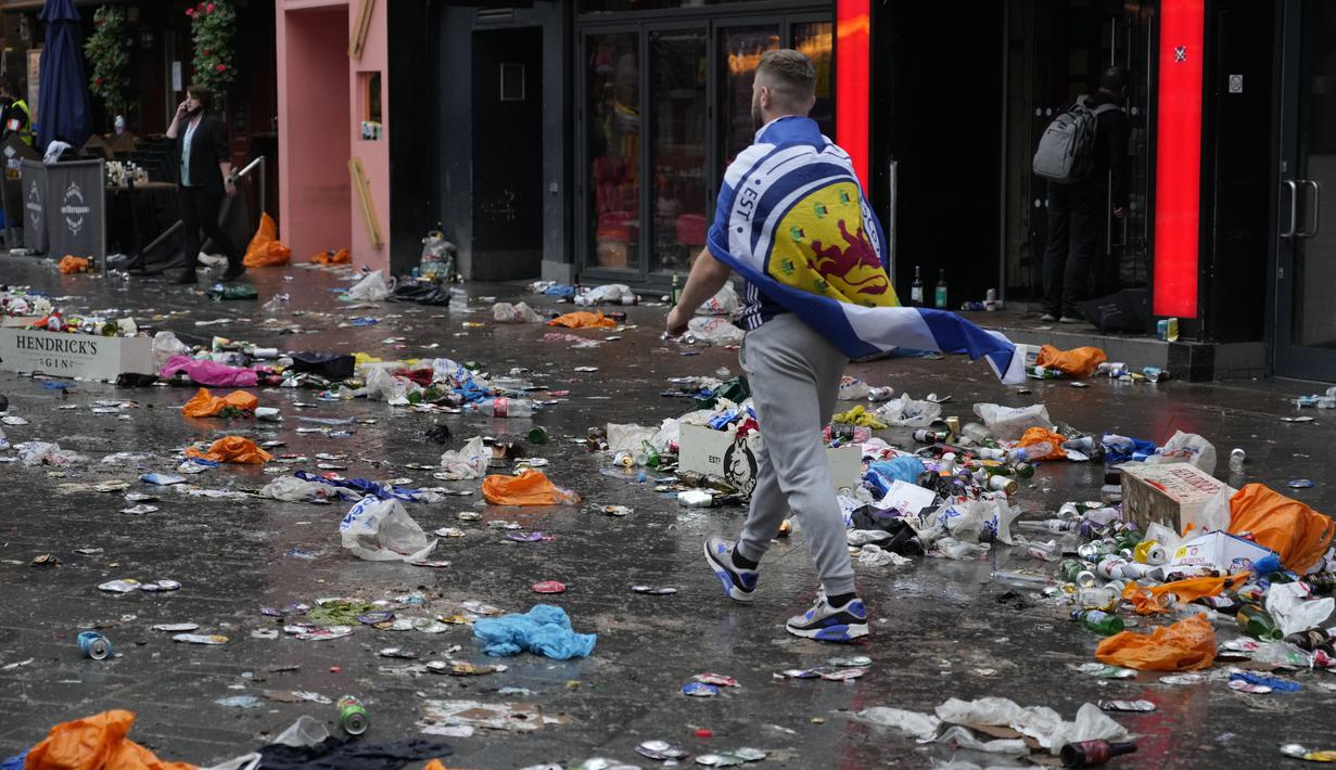 Seorang penggemar Skotlandia berjalan di antara sampah yang ditinggalkan oleh penggemar yang berpesta sebelum pertandingan grup D kejuaraan sepak bola Euro 2020 antara Inggris dan Skotlandia, di London, Jumat (18/6/2021).  (AP Photo/Kirsty Wigglesworth)