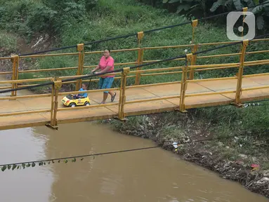 Seorang ibu bersama anaknya melintasi jembatan gantung Kuning yang menghubungkan Pasar Minggu Poltangan ke Cililitan Condet, Jakarta, Selasa (28/12/2021). Jembatan gantung Kuning tersebut merupakan jalan umum dan akses jalan warga yang ingin berlalu-lalang. (merdeka.com/Imam Buhori)