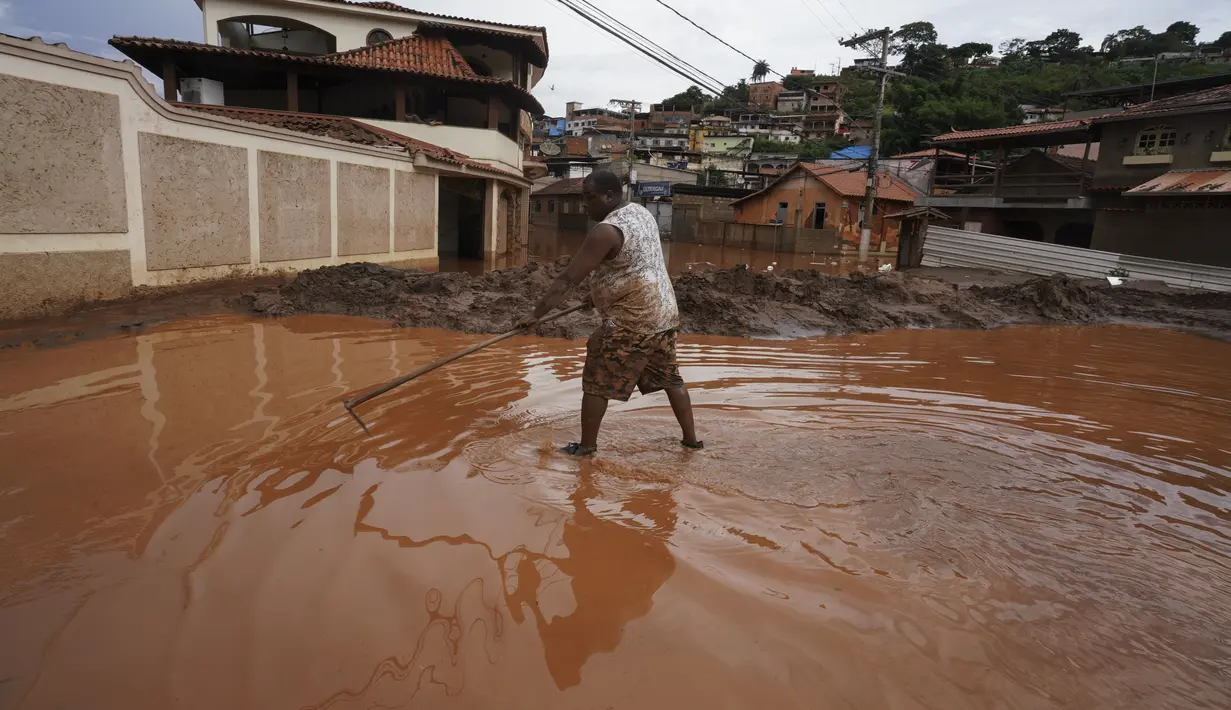 Seorang warga membersihkan lumpur dari jalan setelah banjir di Raposos, negara bagian Minas Gerais, Brasil, Selasa (11/1/2022). Tanah longsor akibat hujan deras telah menewaskan sedikitnya 12 orang dan pihak berwenang sedang memantau bendungan yang bisa jebol. (AP Photo/Eugenio Savio)