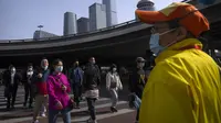 Komuter yang mengenakan masker berjalan melintasi persimpangan di kawasan pusat bisnis di Beijing, Selasa (12/4/2022). AS telah memerintahkan semua staf konsuler non-darurat untuk meninggalkan Shanghai, yang dikunci ketat untuk menahan lonjakan COVID-19. (AP Photo/Mark Schiefelbein)