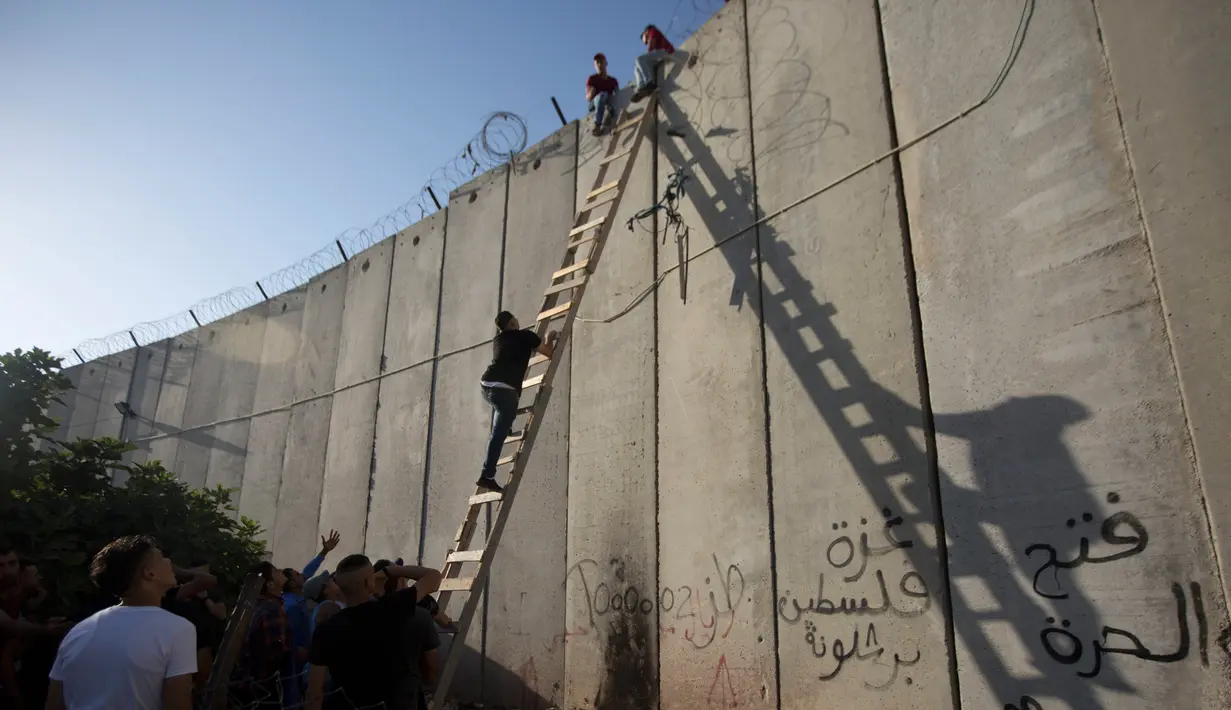 Suasana saat pemuda Palestina menggunakan tangga saat memanjat tembok pembatas Israel dalam perjalanan menuju Masjid Al Aqsa untuk mengikuti salat Jumat terakhir di bulan Ramadhan, Al-Ram, Utara Yerusalem, Jumat (8/6). (AP Photo/Majdi Mohammed)