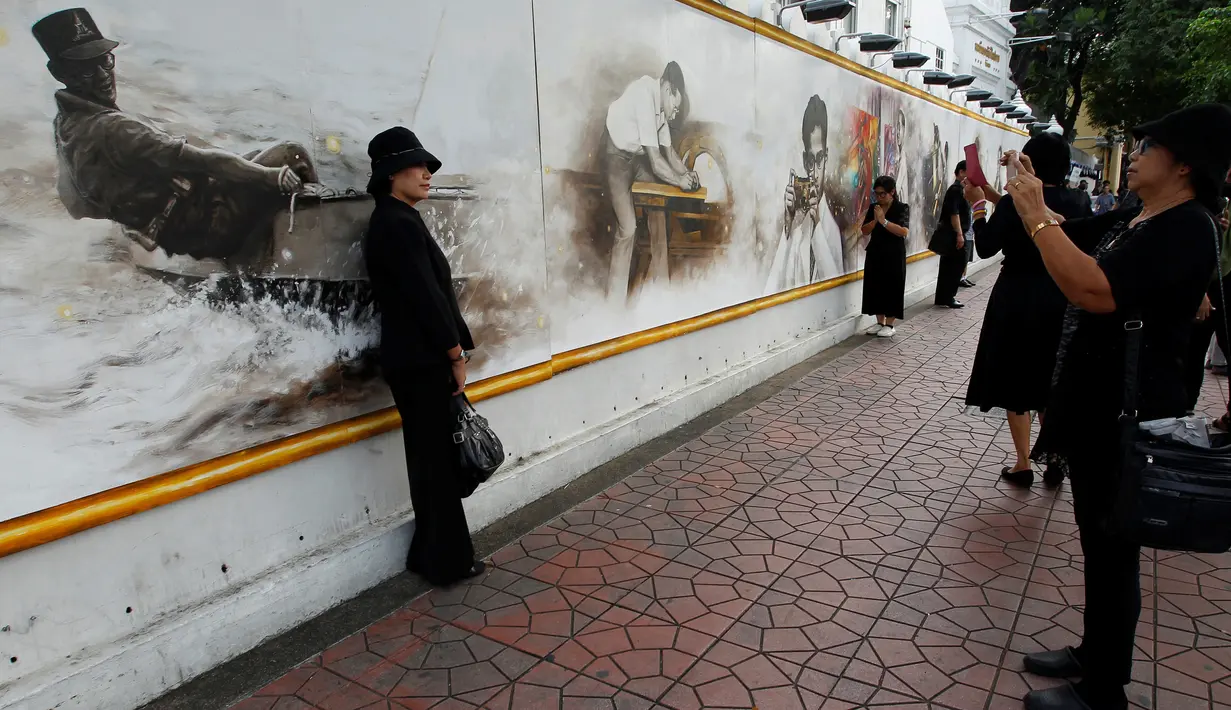 Seorang wanita diambil gambarnya dengan latar belakang gambar Raja Bhumibol Adulyadej dekat Grand Palace di Bangkok, Thailand, Rabu (19/10). Untuk menghormati Raja Bhumibol Adulyadej, Grand Palace dipasangi gambarnya. (REUTERS / Chaiwat Subprasom)