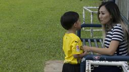Anak dari Stefano Teco, yang bernama Romario, bersama ibunya, Miranda, saat latihan Persija Jakarta di Lapangan Sutasoma, Jakarta, Minggu (25/2/2018). Ketika ayahnya bekerja sang anak asyik bermain sepak bola. (Bola.com/Aspirilla Dwi Adha)