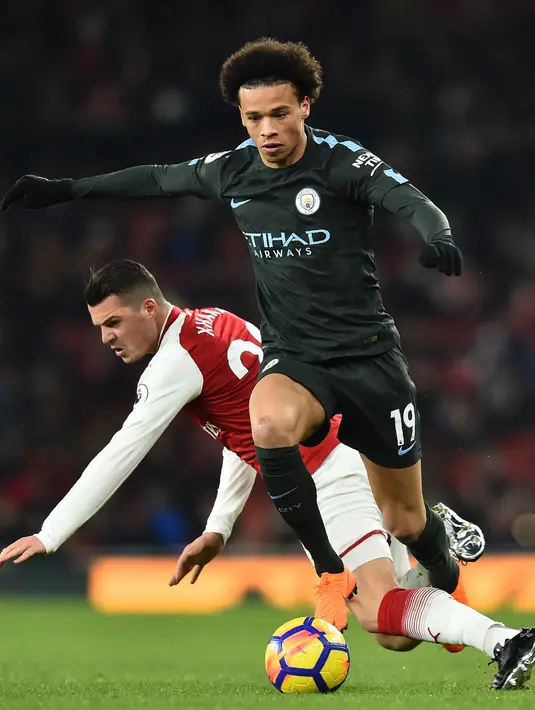 Gelandang Manchester City Leroy Sane berebut bola dengan pemain Arsenal, Granit Xhaka pada laga pekan ke-28 Premier League di Emirates Stadium,  Jumat (2/3). Tampil di kandang lawan, Manchester City melibas Arsenal dengan skor 3-0. (Glyn KIRK/AFP)