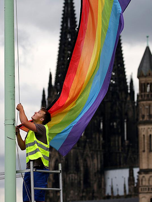 Seorang pria mengibarkan bendera warna pelangi usai pengumuman legalisasi undang-undang pernikahan sesama jenis di Cologne, Jerman (30/6). (AFP PHOTO / DPA / Oliver Berg / Germany OUT)