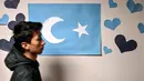 Seorang siswa Uighur melintasi bendera Uighur yang terpajang pada salah satu sudut sekolah di distrik Silivri, Istanbul, Turki (29/12/2019). (AFP/Ozan Kose)