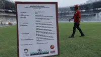 Pekerja melintas di depan papan spesifikasi rumput  di SUGBK, Senayan, Jakarta, Selasa (8/8/2017). SUGBK menggunakan rumput jenis Zoysia matrella yang merupakan rumput standar FIFA untuk stadion bertaraf internasional. (Bola.com/M Iqbal Ichsan)