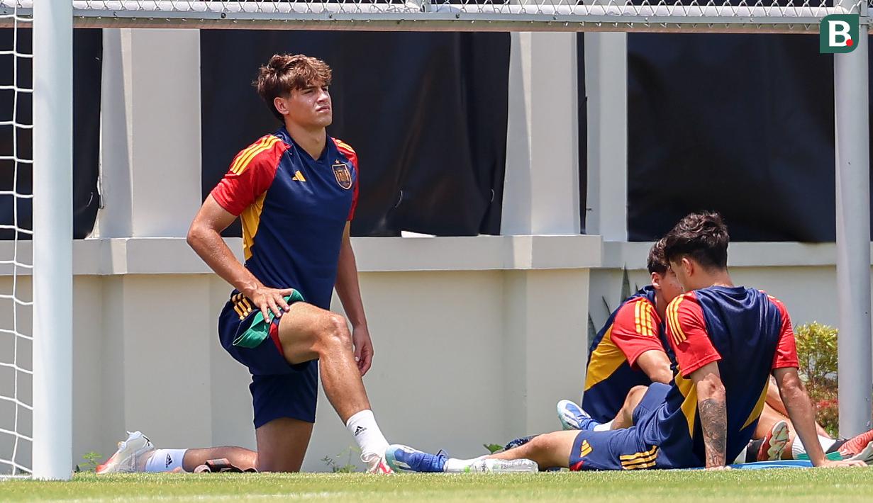Ekspresi pemain Timnas Spanyol U-17, Marc Guiu (kiri), saat melakukan peregangan otot bersama rekannya dalam menjalani latihan dibawah sinar terik matahari yang berlangsung di Lapangan Sriwaru, Kecamatan Laweyan, Kota Solo, Rabu (8/11/2023). (Bola.com/Radifa Arsa)